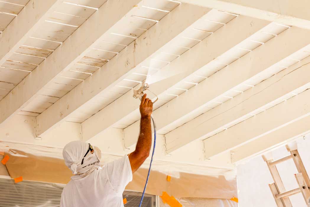 a contractor spraying a fresh coat of paint to this beamed commercial property ceiling in Miramar FL