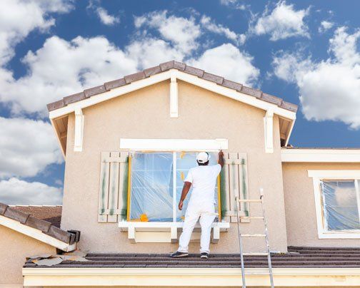 local painter standing on the roof to paint the second floor of this two-story house in Miramar FL